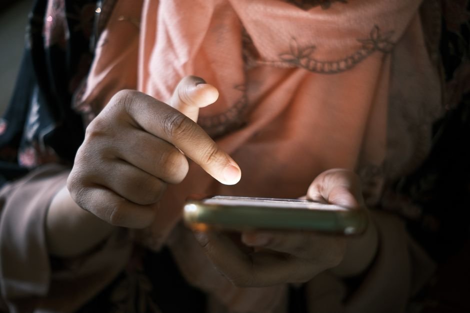 Procès Siri IA : Apple va payer 250 millions de dollars aux propriétaires d’iPhone Main tenant un smartphone en gros plan, illustrant le règlement du procès Siri IA d'Apple