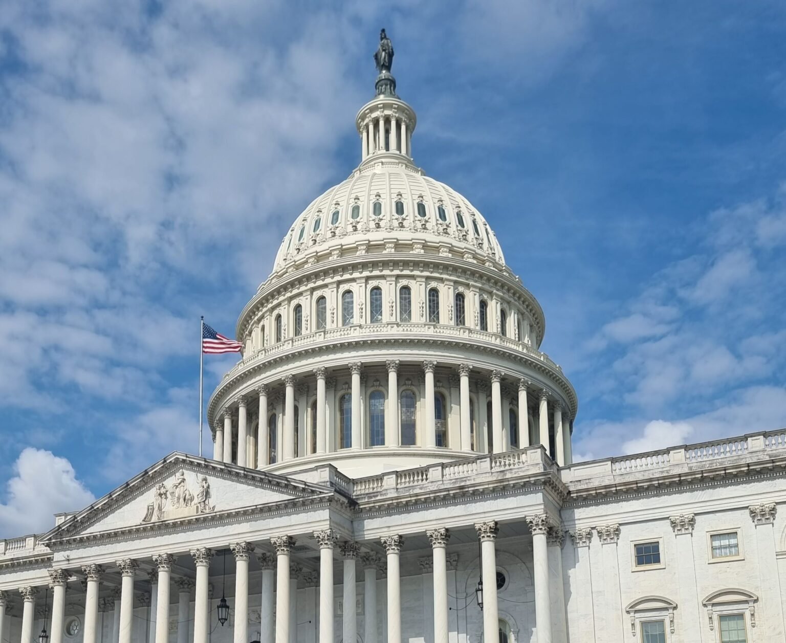 Le dôme du Capitole des États-Unis à Washington sous un ciel bleu, avec le drapeau américain