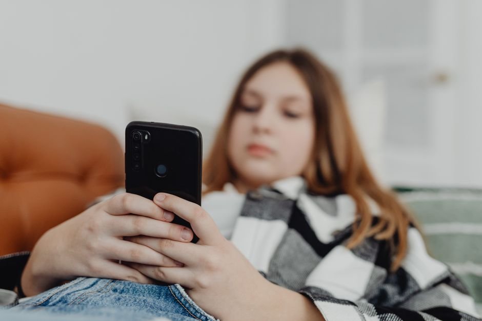 OpenAI lance une notification parentale ChatGPT après un bannissement pour violence Adolescente allongée utilisant son smartphone, illustrant l'usage de ChatGPT par les jeunes